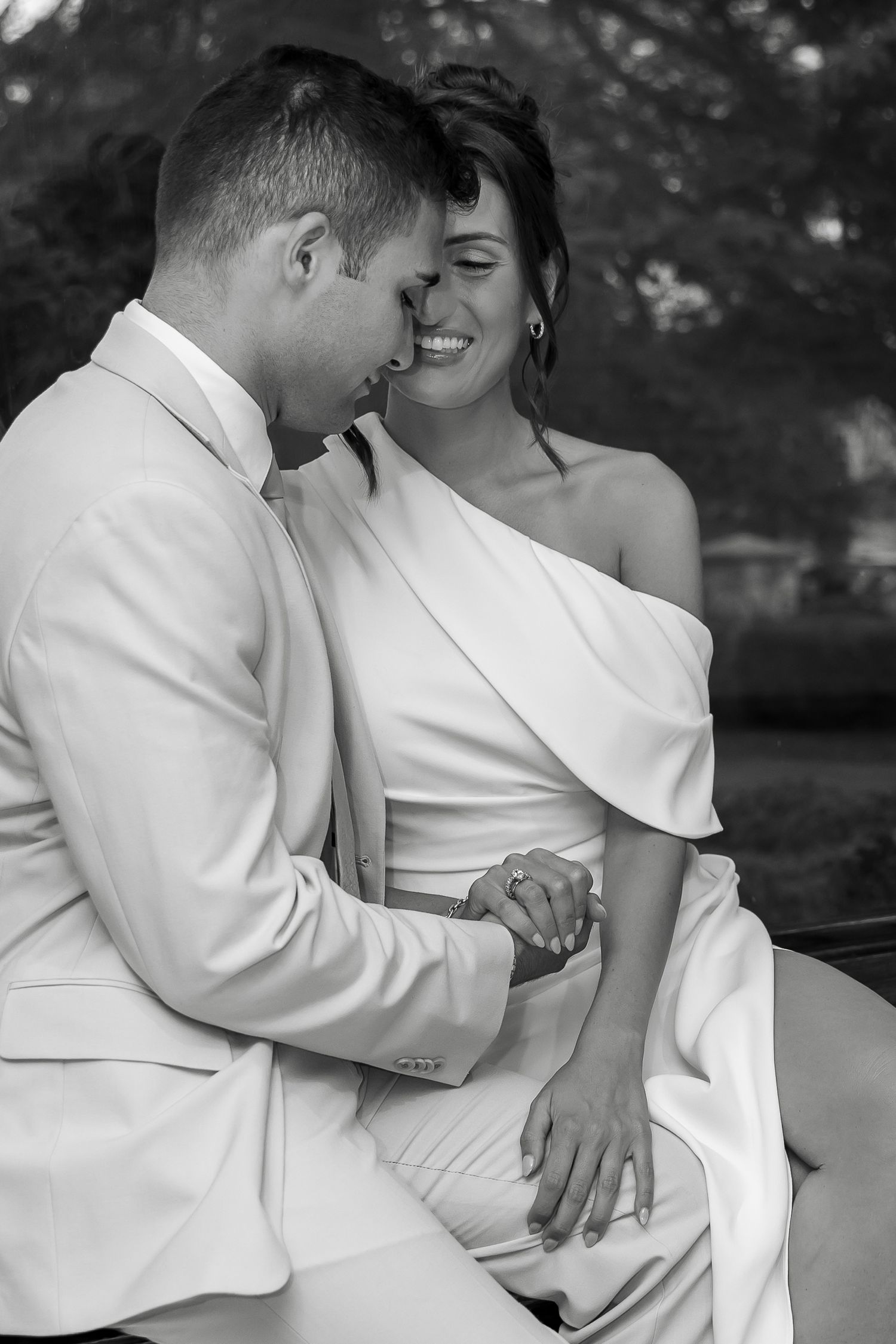 An intimate black and white portrait of a couple in white formal attire sharing a tender moment.
