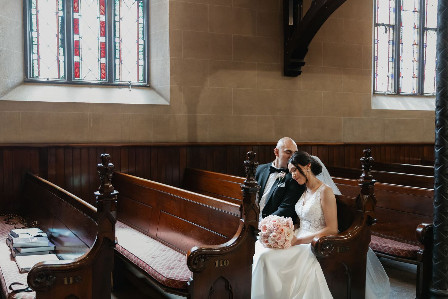 A couple sits together in wooden church pews during an intimate ceremony.