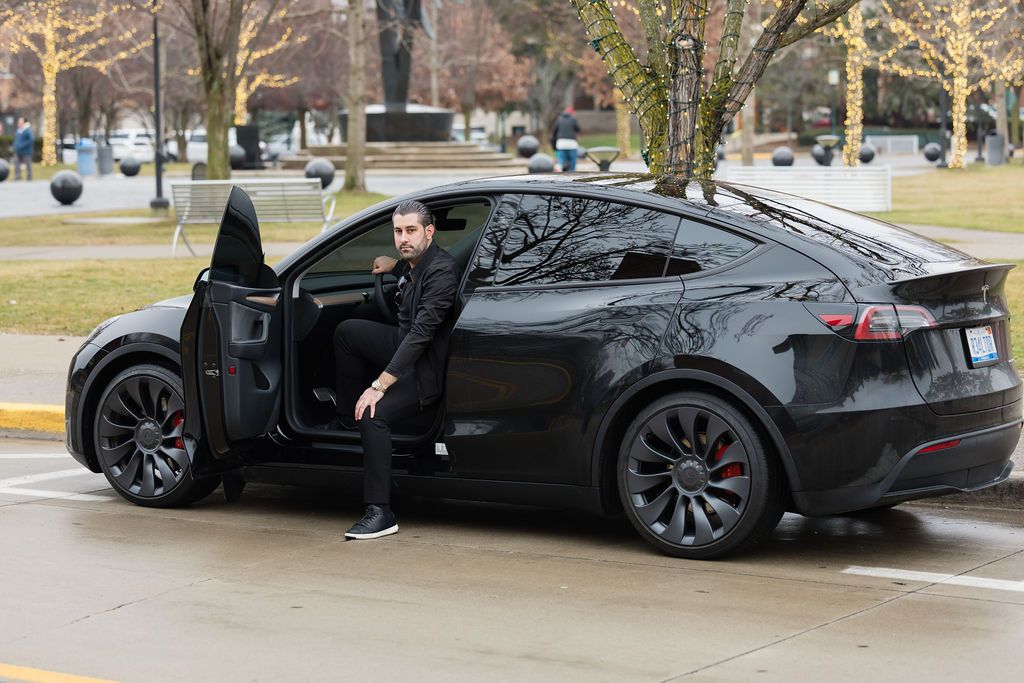 Black Tesla Model X SUV parked on street with open falcon wing door and someone getting out of vehicle.