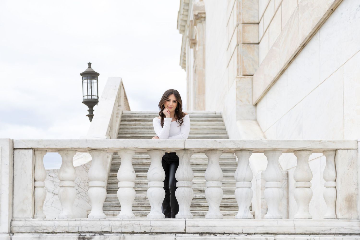A person sitting on white stone balustrade stairs with classic architecture details.