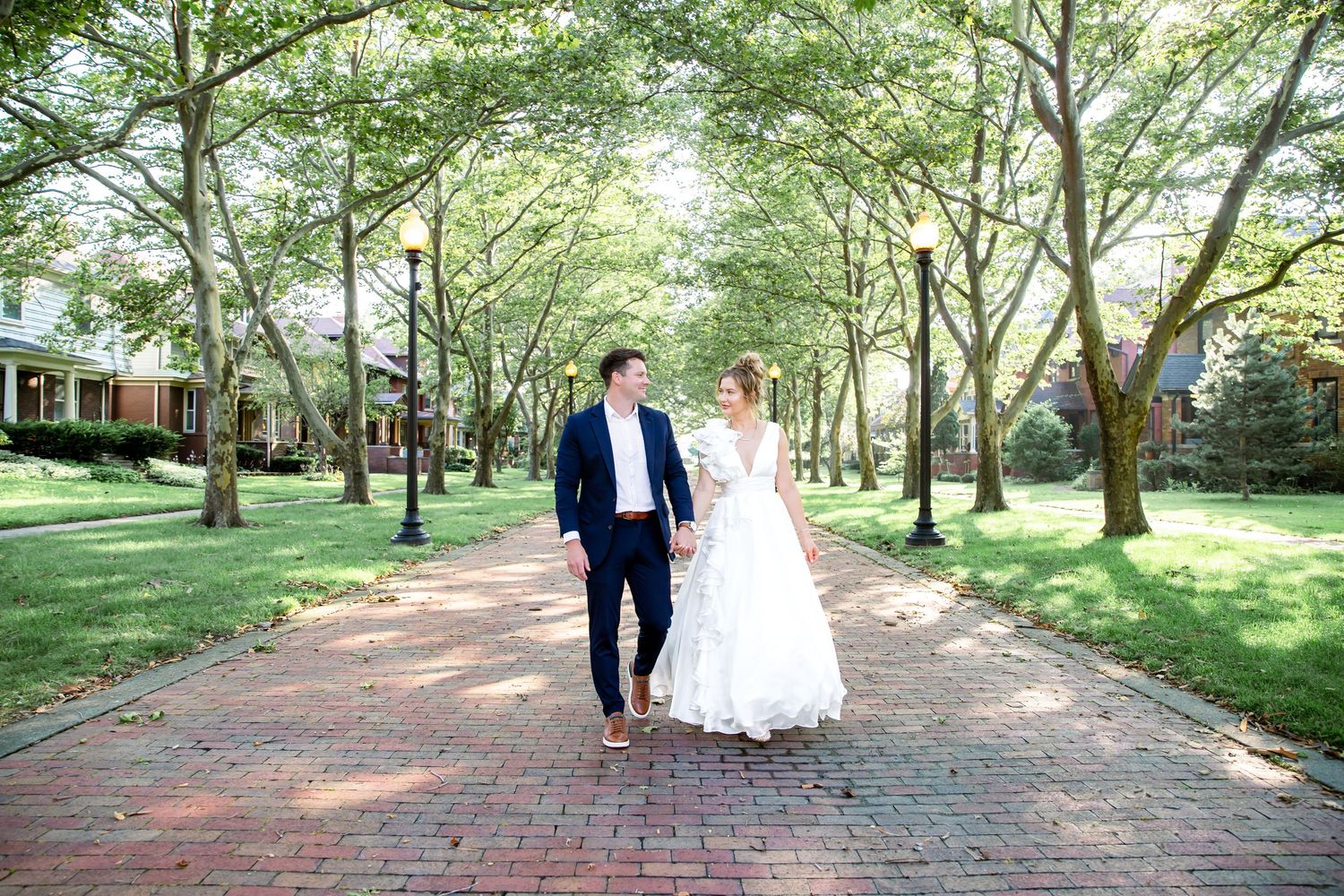 A sunny wedding day stroll down a tree-lined brick pathway.