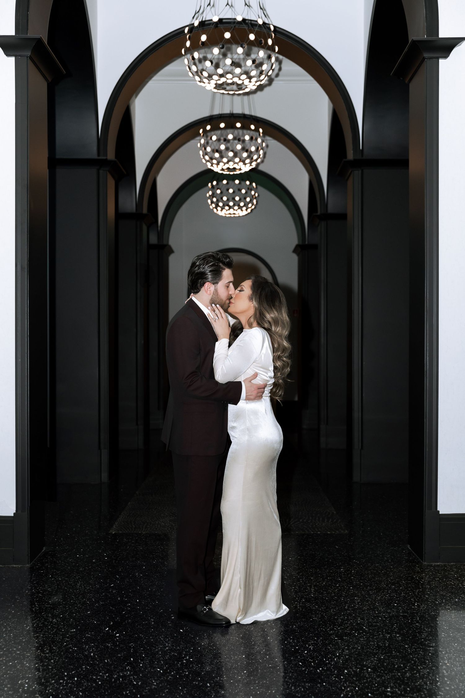 A romantic wedding portrait under elegant arches with hanging crystal chandeliers.