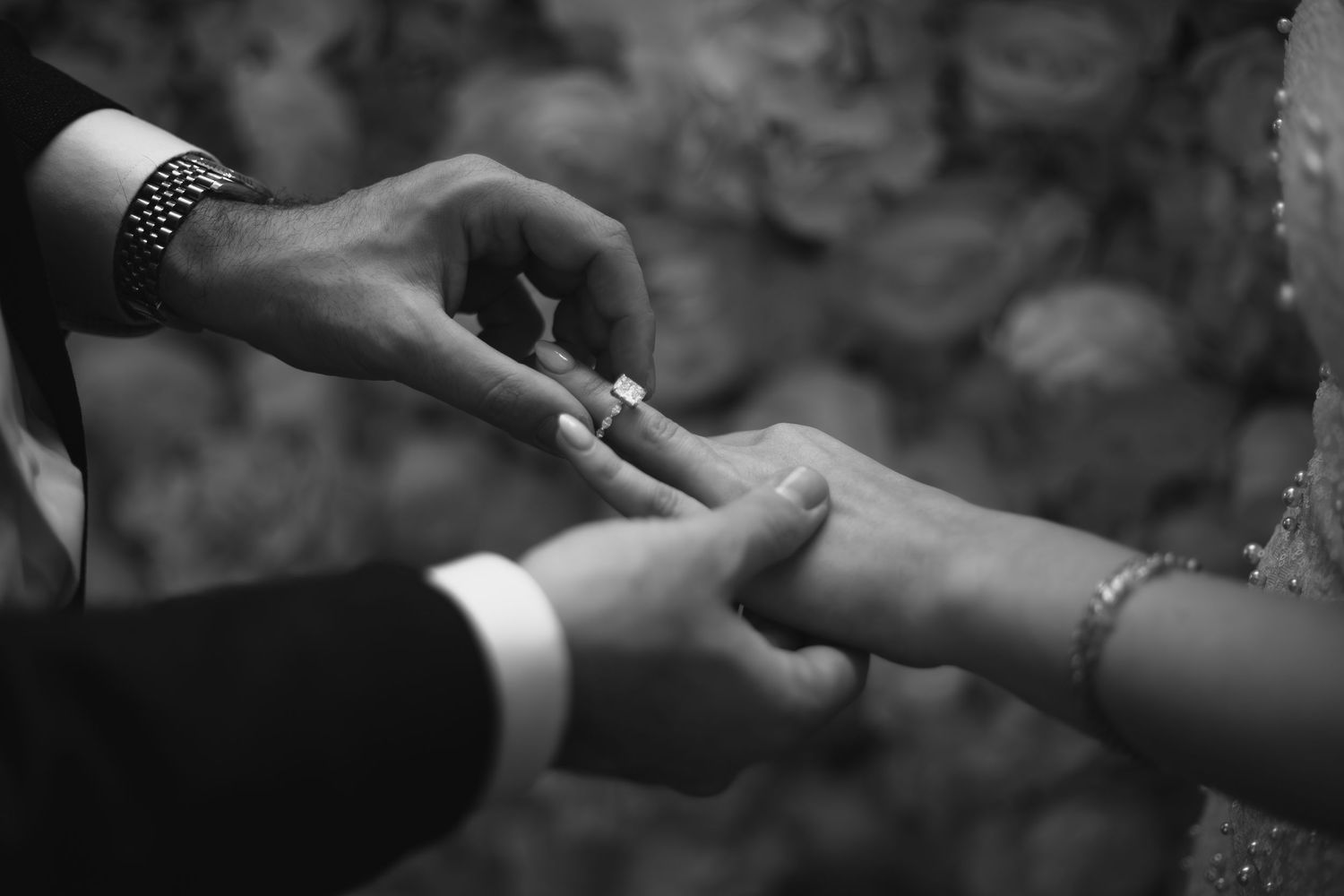 A black and white close-up of hands exchanging wedding rings during a ceremony.