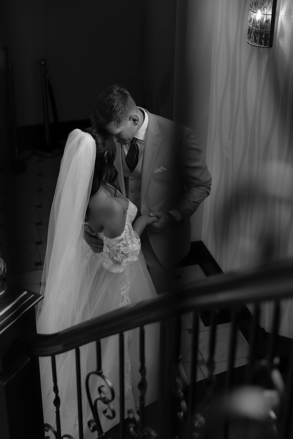 Dramatic black and white wedding moment captured on an elegant staircase with flowing veil.