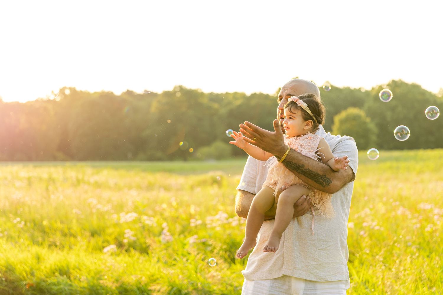 A joyful figure plays with bubbles in a sunlit meadow during golden hour while wearing white clothing.