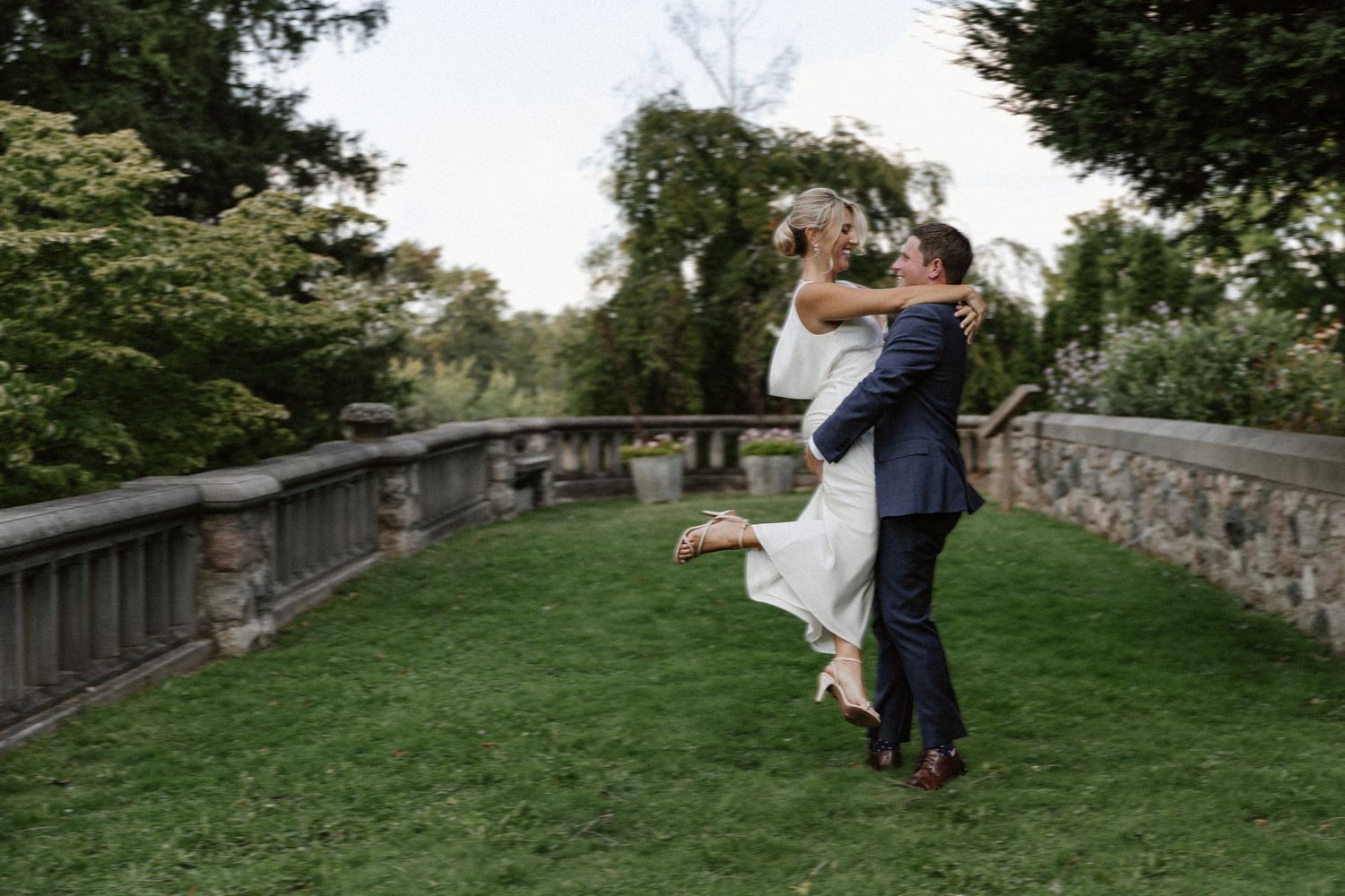 A joyful wedding couple sharing a playful moment on a stone balcony surrounded by greenery.