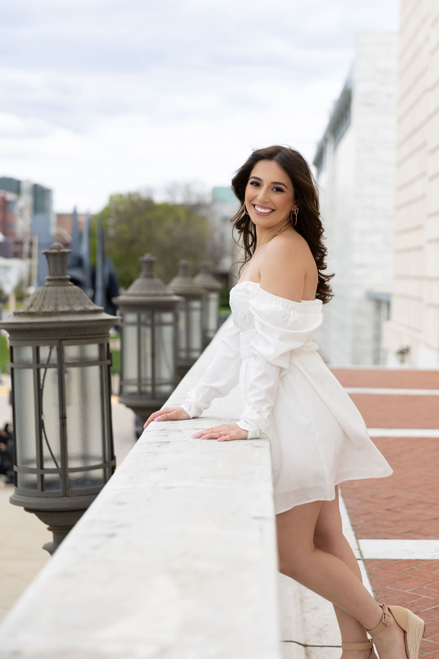 Woman in white dress leans against railing with decorative lanterns in urban setting.
