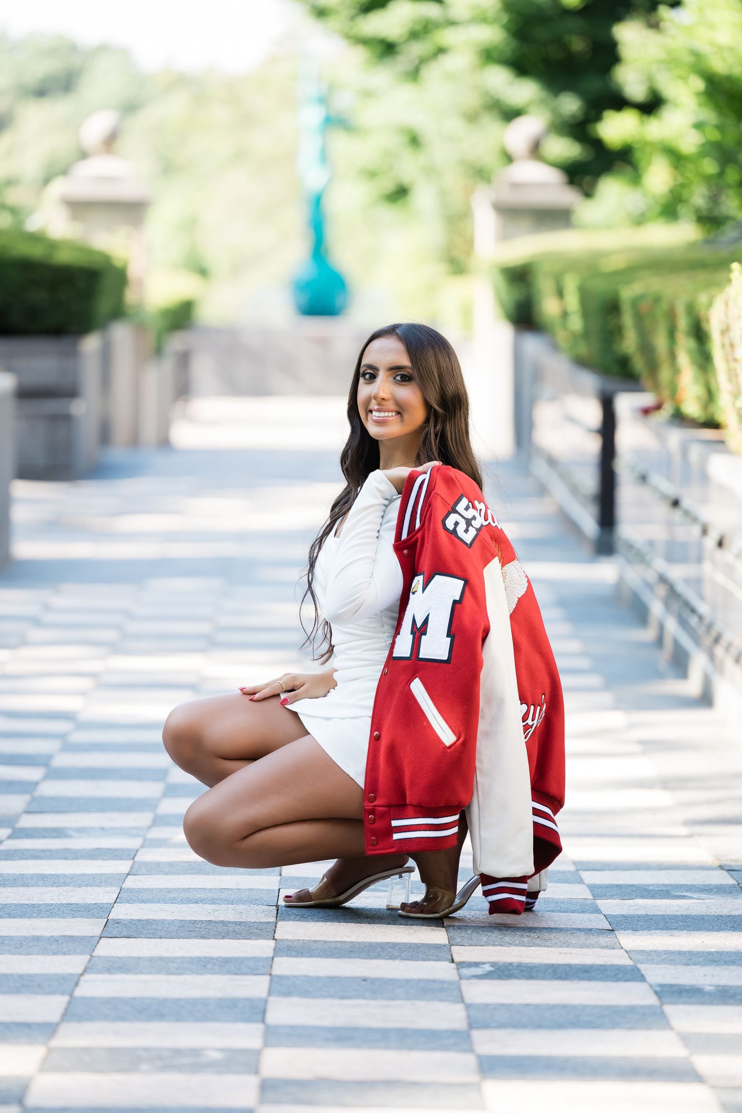 Woman in white outfit with red varsity jacket posing on checkered pathway.