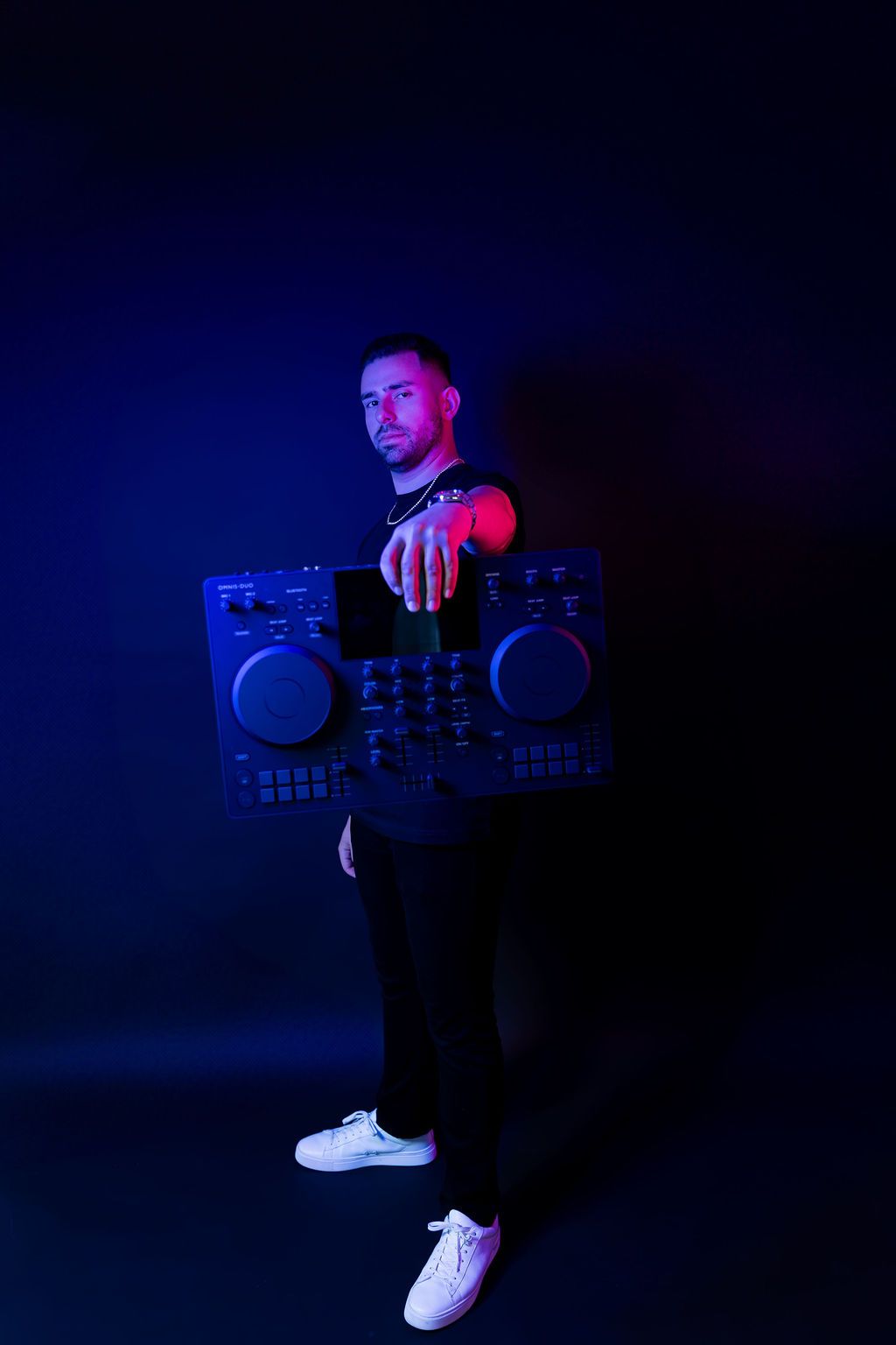 DJ with professional equipment posing in dark room with dramatic blue and purple lighting effects.