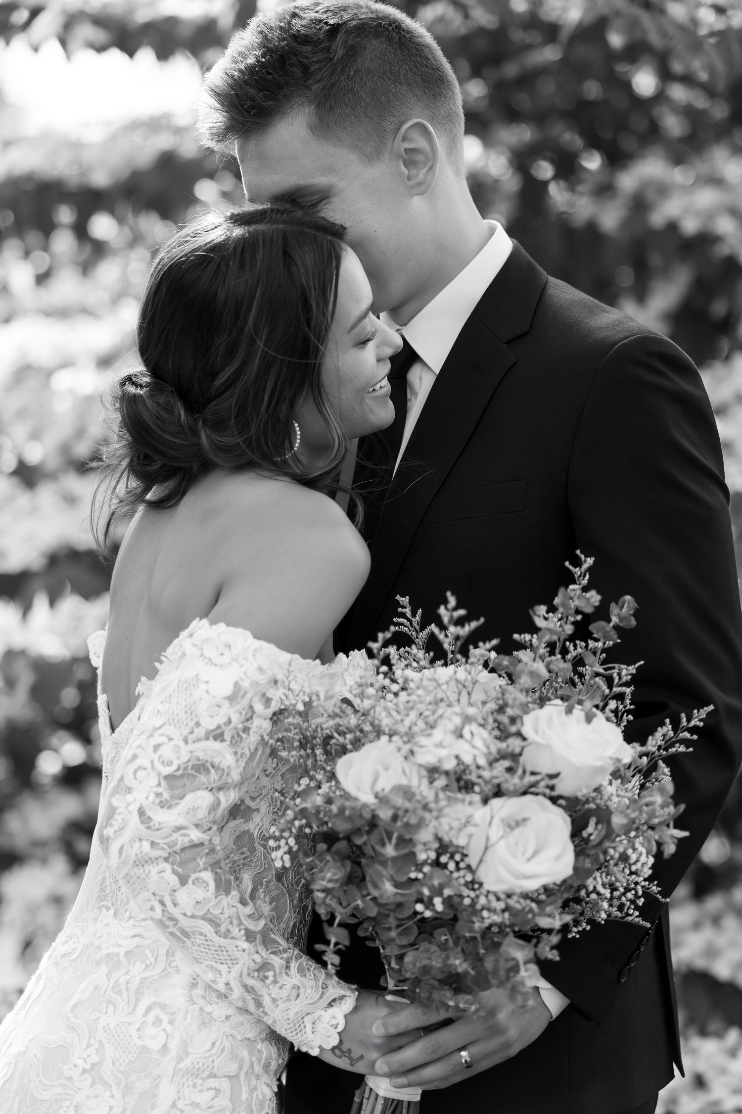 Black and white portrait of newlyweds embracing with bridal bouquet of roses and greenery.