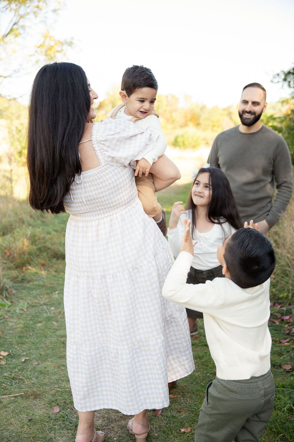 A family enjoying a playful moment together outdoors in autumn with warm golden light filtering through the trees.
