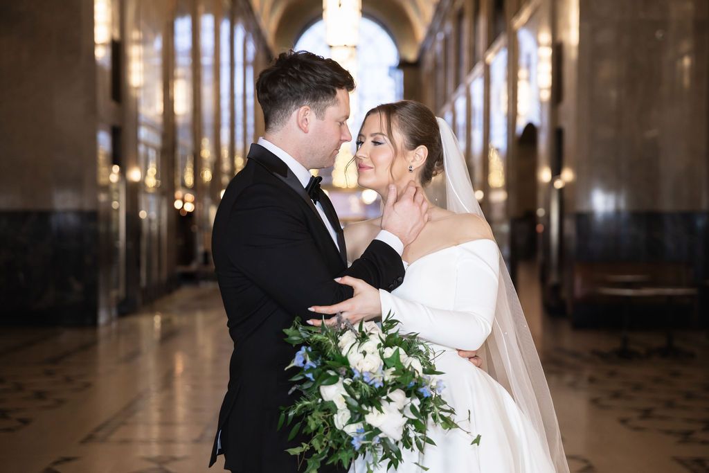 A romantic wedding moment captured in an elegant cathedral hallway with white flowers and dramatic lighting.