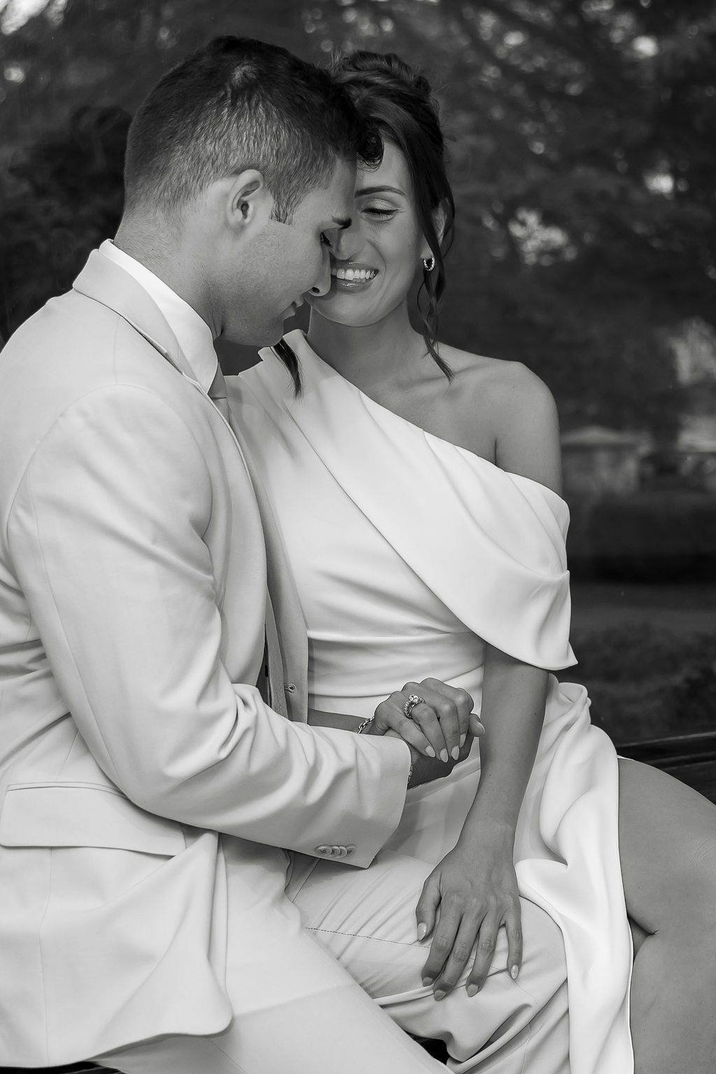 An intimate black and white portrait of a couple in white attire sharing a tender moment outdoors.