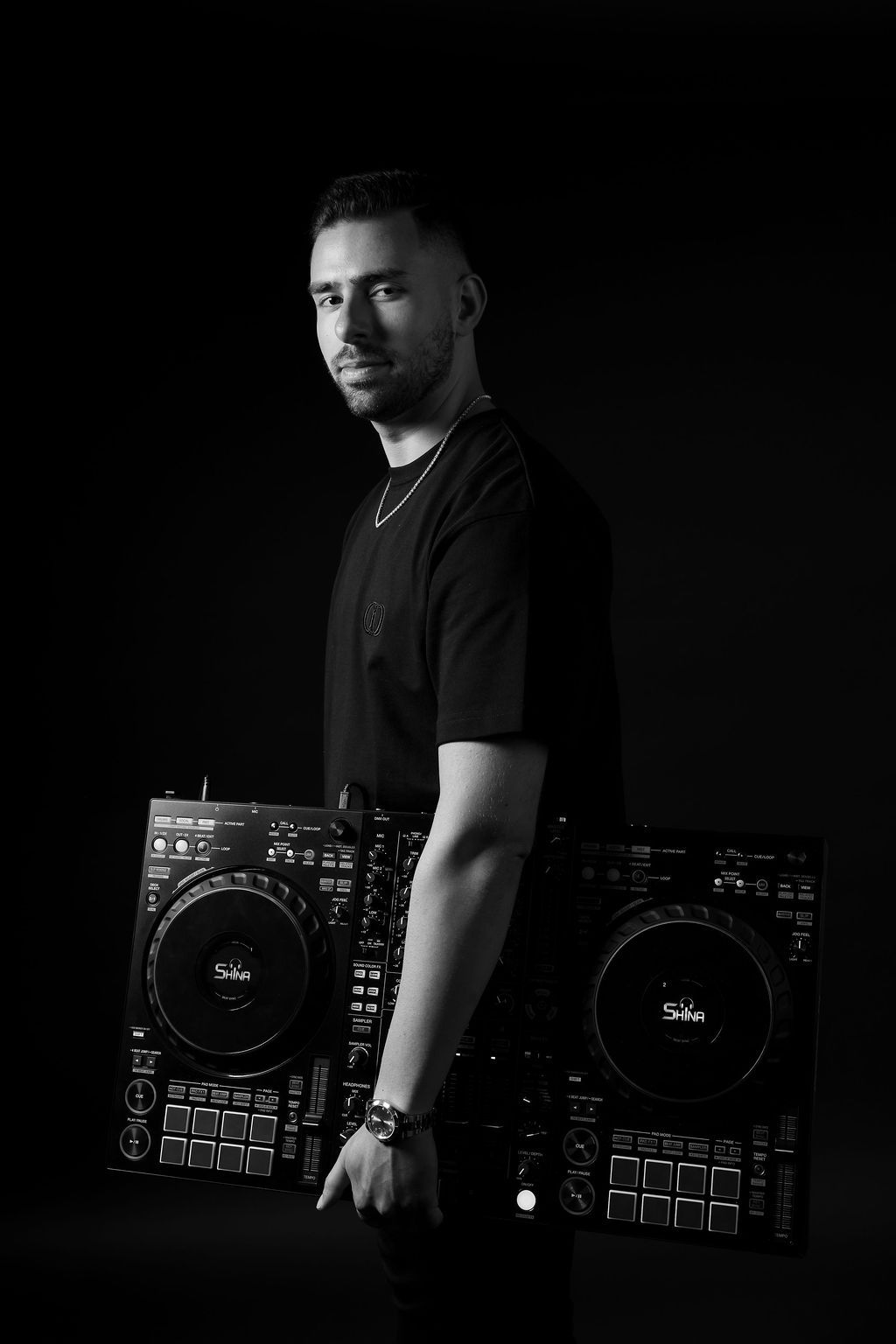 DJ poses with professional mixing equipment in dramatic black and white studio portrait.