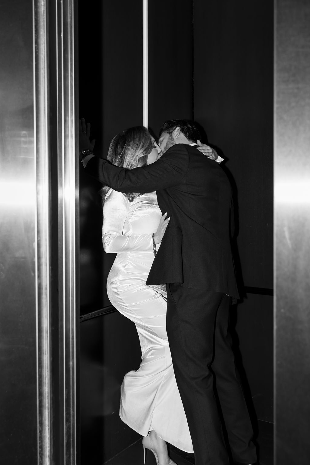 A couple sharing a passionate kiss outside elevator doors in black and white photography.