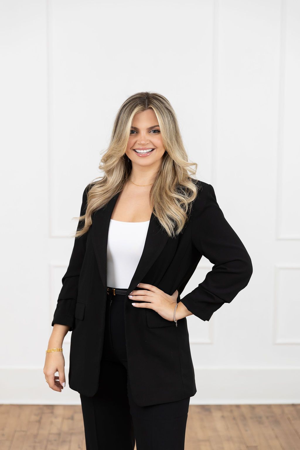 Professional business woman in black blazer and pants smiling confidently while posing against white background.