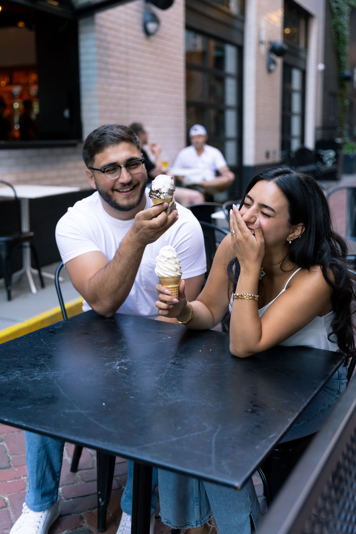 Happy couple laughing while eating ice cream together at an outdoor cafe table.