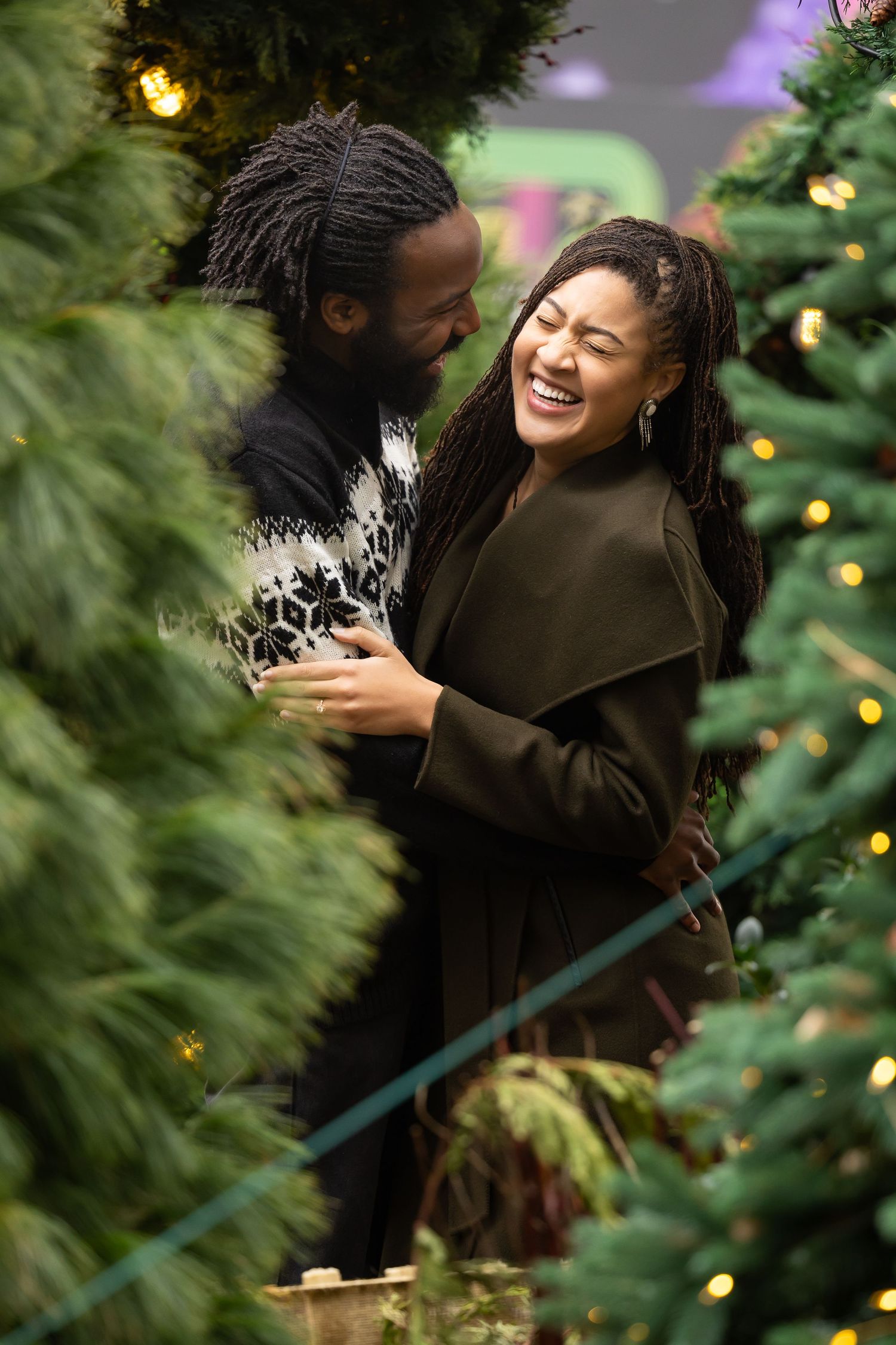 A couple shares a joyful moment among Christmas trees with twinkling lights.