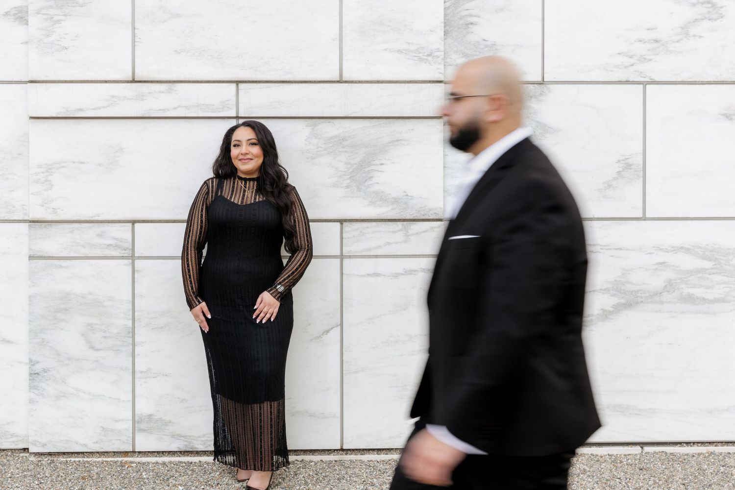 A couple in formal wear poses artistically against white stone wall.