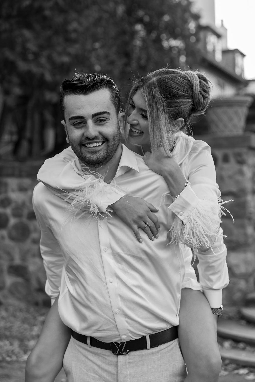 A joyful black and white photo of a piggyback ride moment between a couple in white attire.