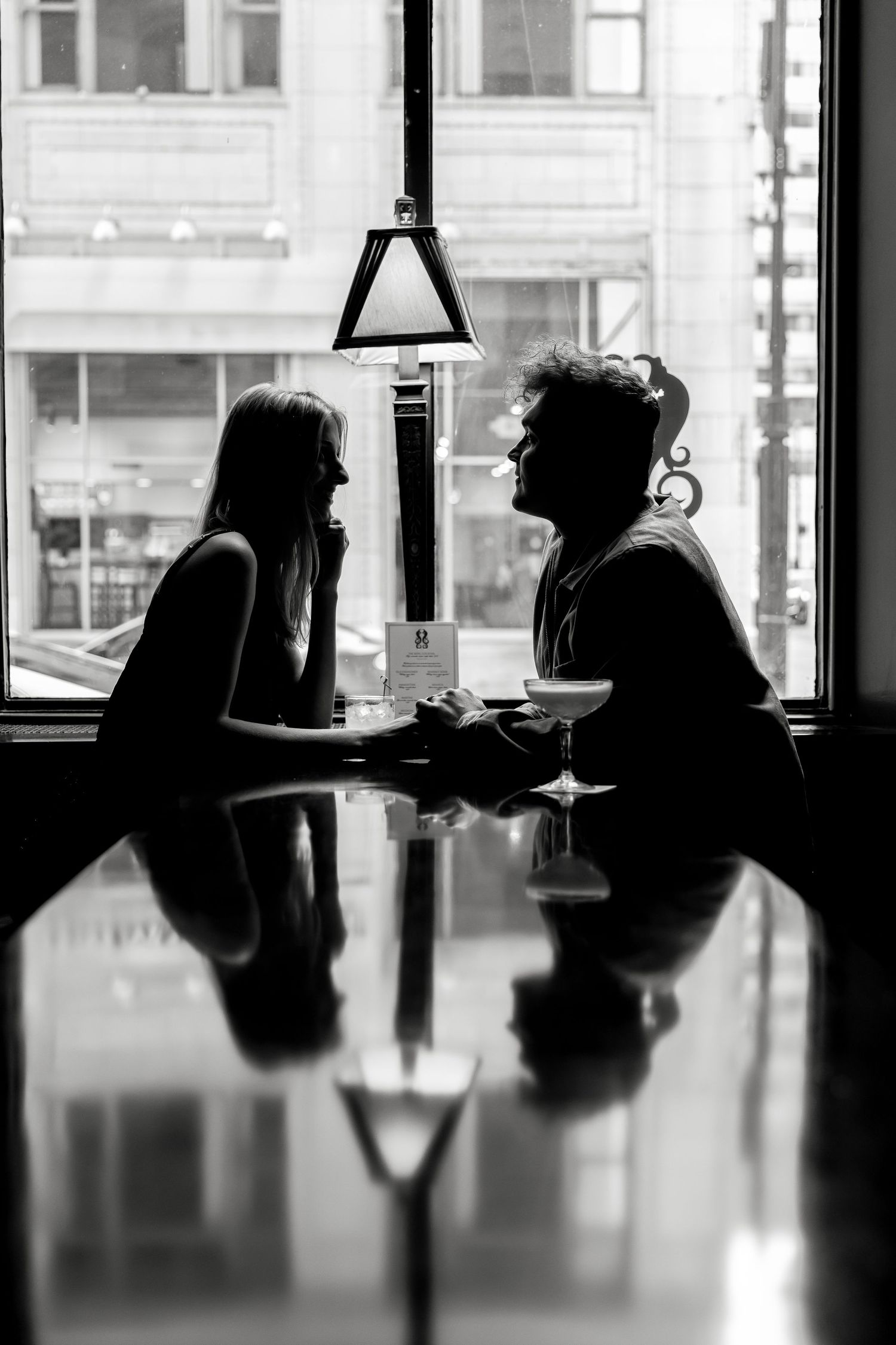 A couple shares a romantic moment at a cafe table by a window in black and white.