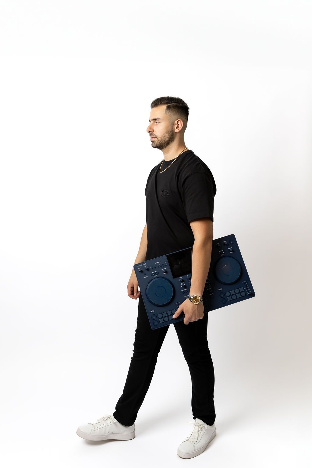Professional DJ carrying music equipment while dressed in black against a white studio background.