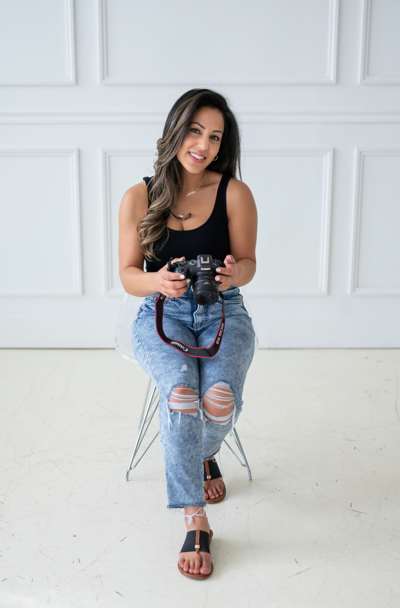 Professional photographer in relaxed pose holding camera while sitting on modern chair.
