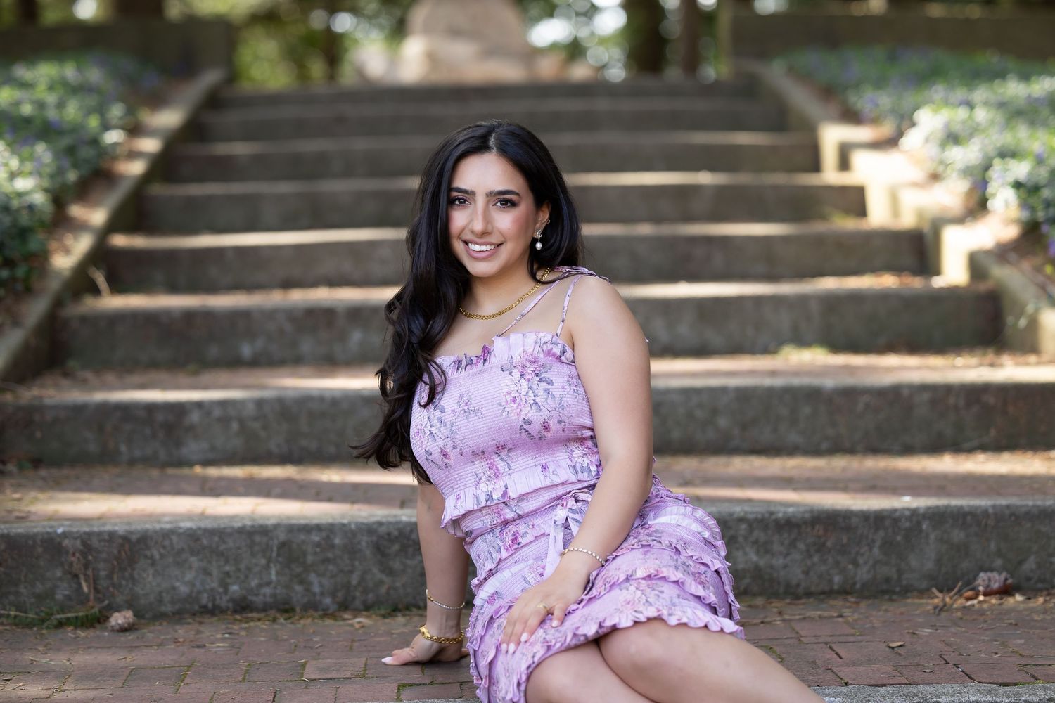 Woman in lavender dress poses elegantly on outdoor stone staircase.