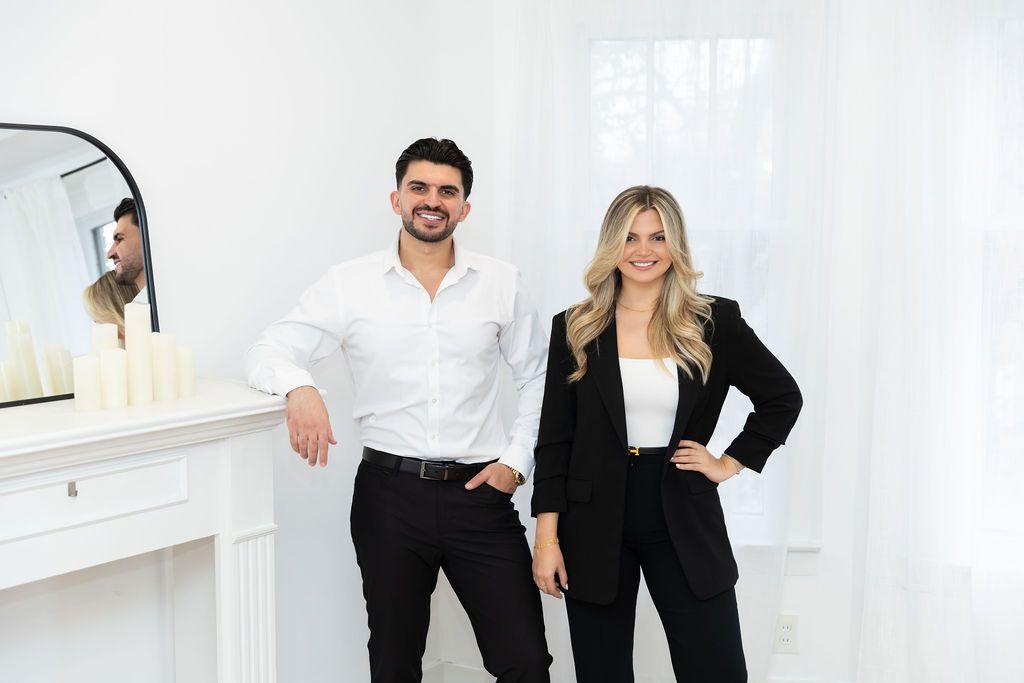 Two entrepreneurs in business attire posing together in modern white office space.