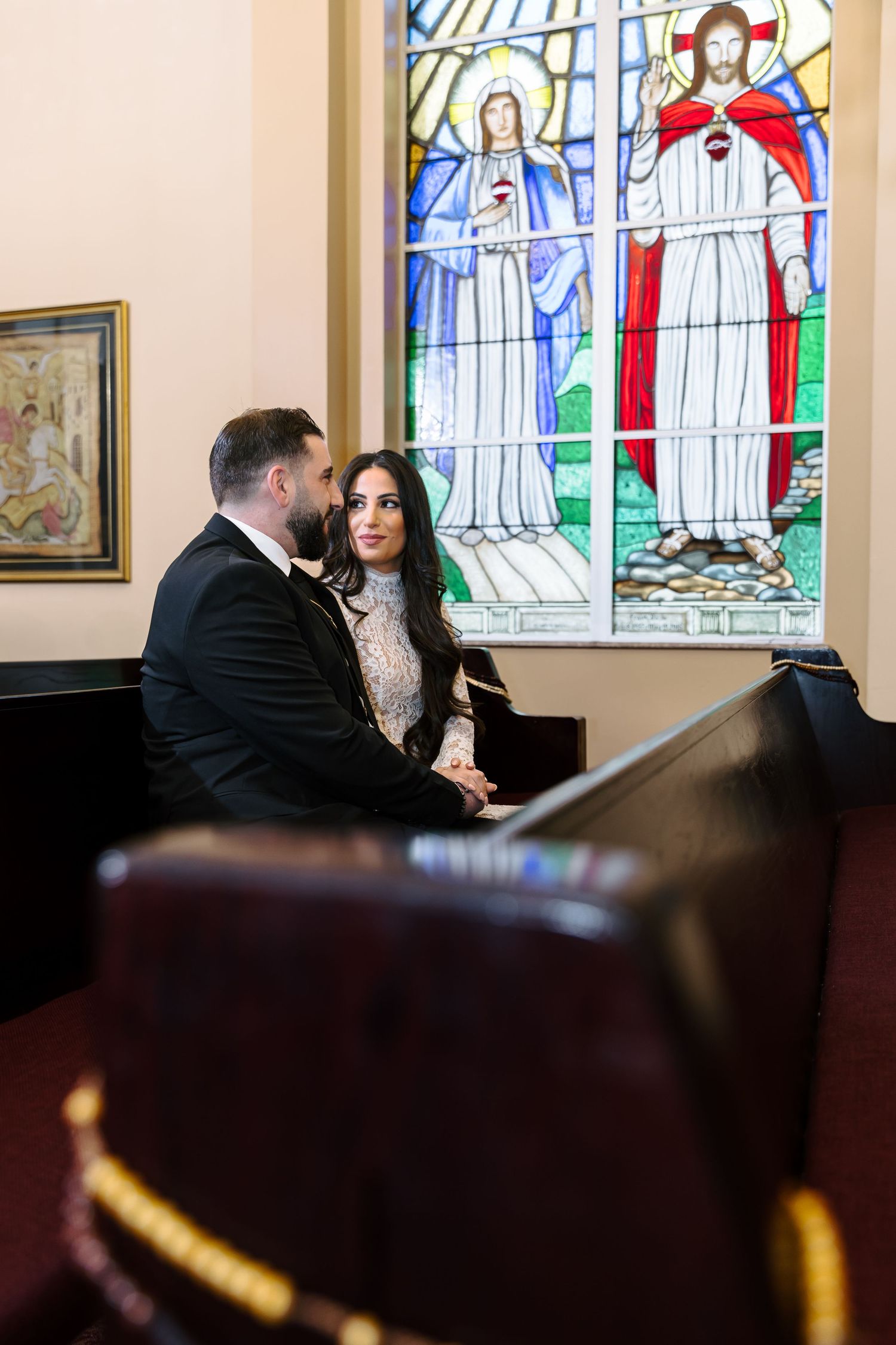 A tender moment shared near colorful stained glass religious windows and dark leather furniture.