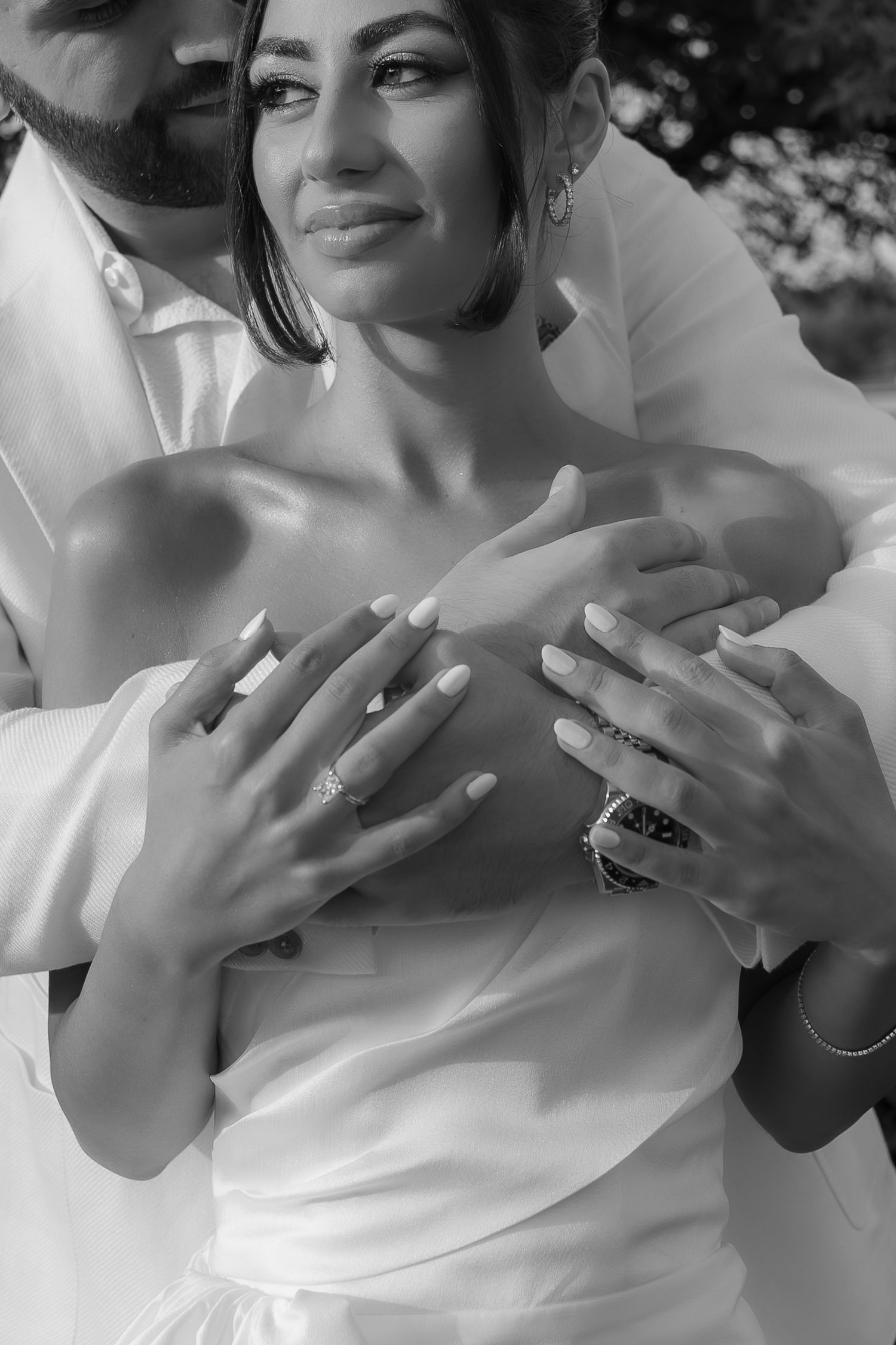 Close-up portrait showing hands with rings and wedding attire in black and white.