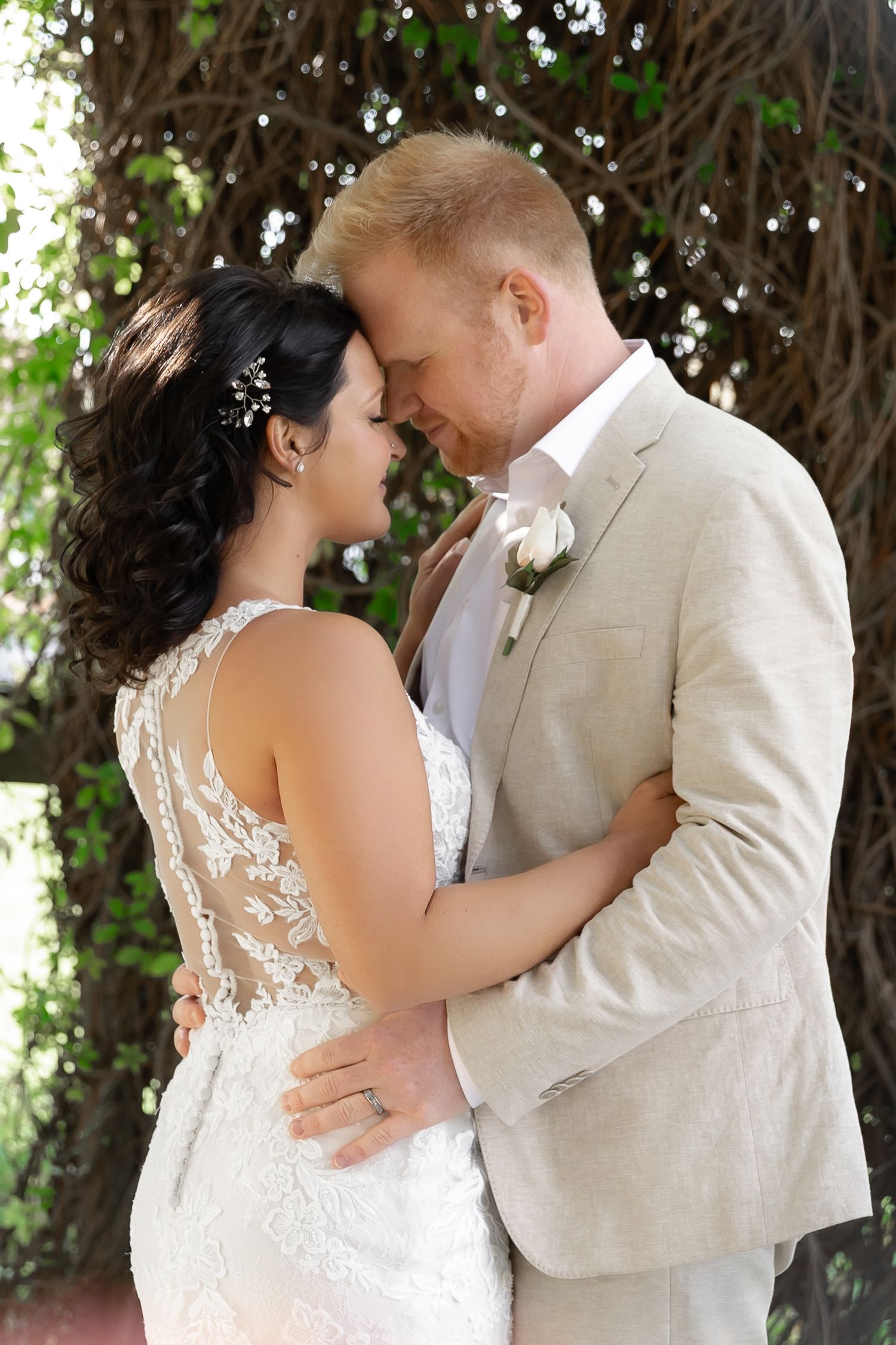 A romantic moment between newlyweds standing together under lush greenery.