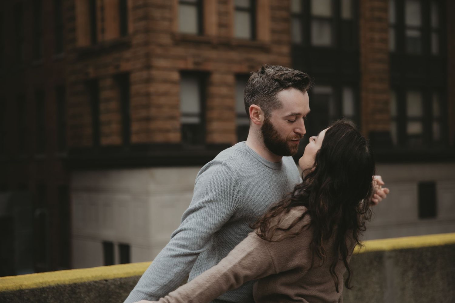 A couple shares an intimate embrace against brick building background.
