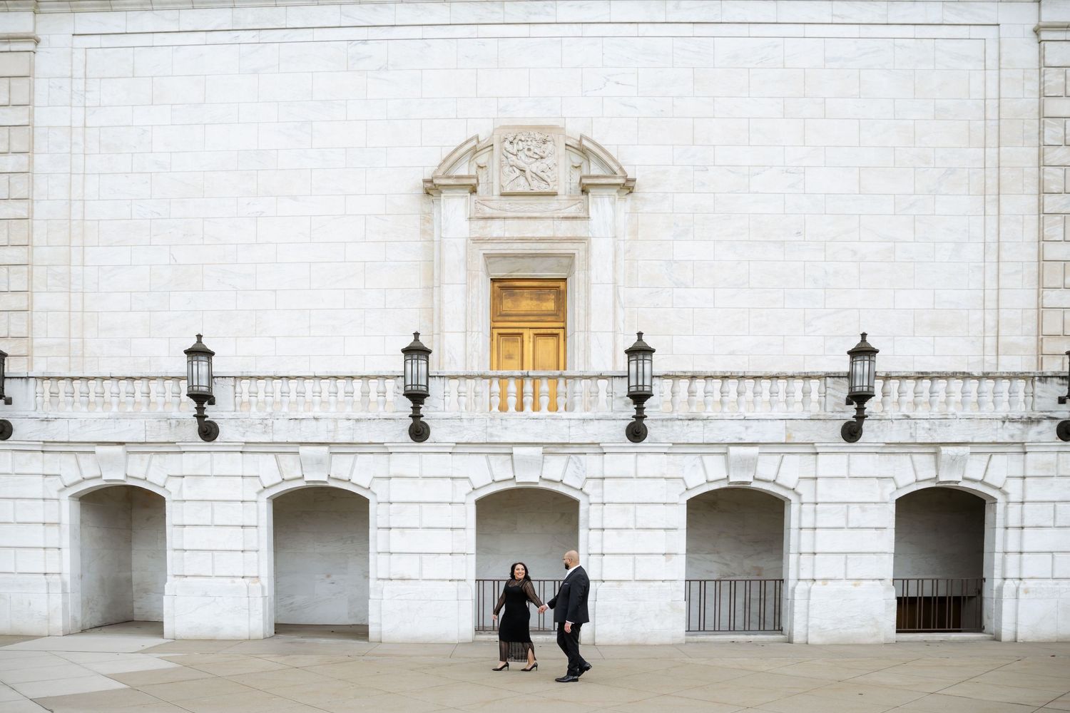 Two figures stand beneath ornate white architecture with golden door and lanterns.