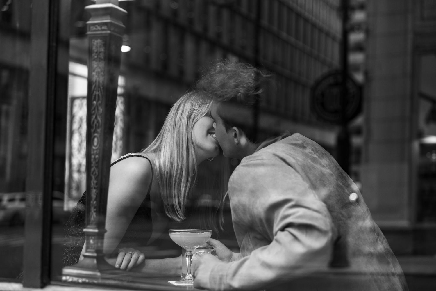 A couple sharing a close moment viewed through a cafe window in black and white photography.