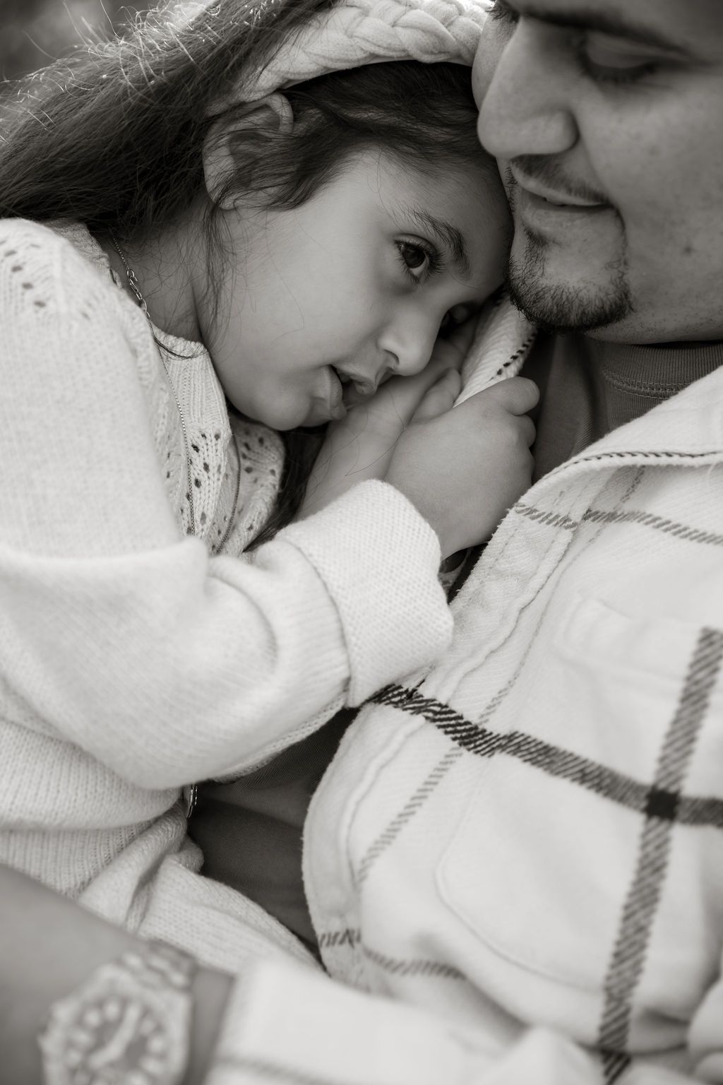 A tender black and white portrait showing a close embrace between two people wearing white sweaters.