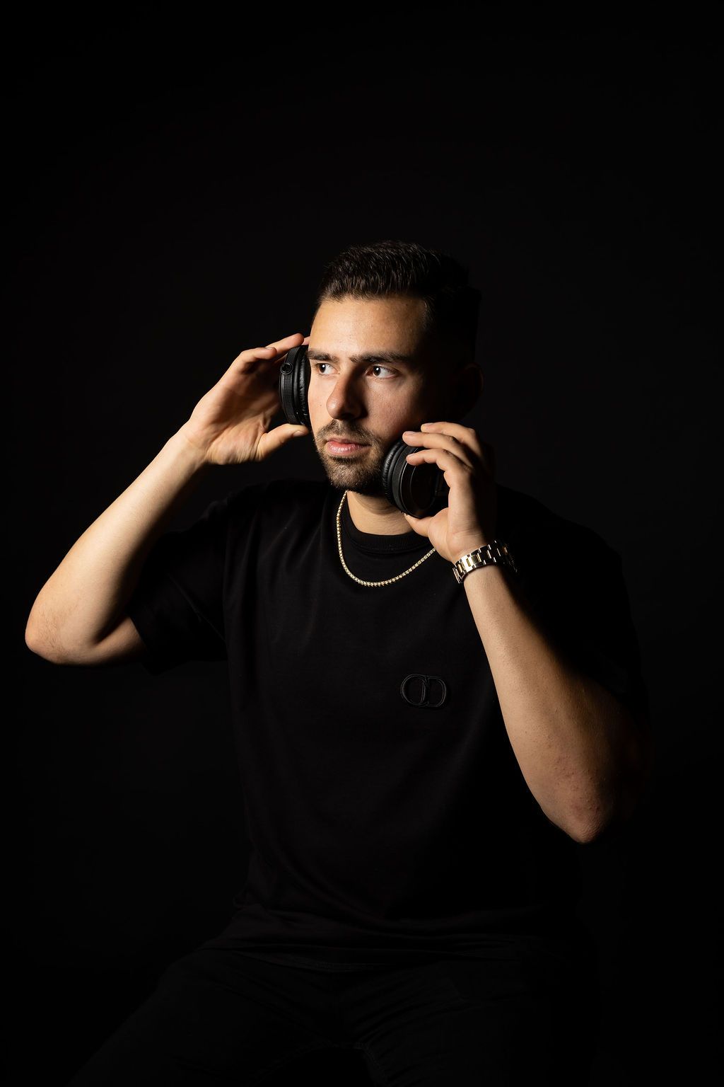 Low key studio portrait showing person in black shirt holding headphones against dark background.