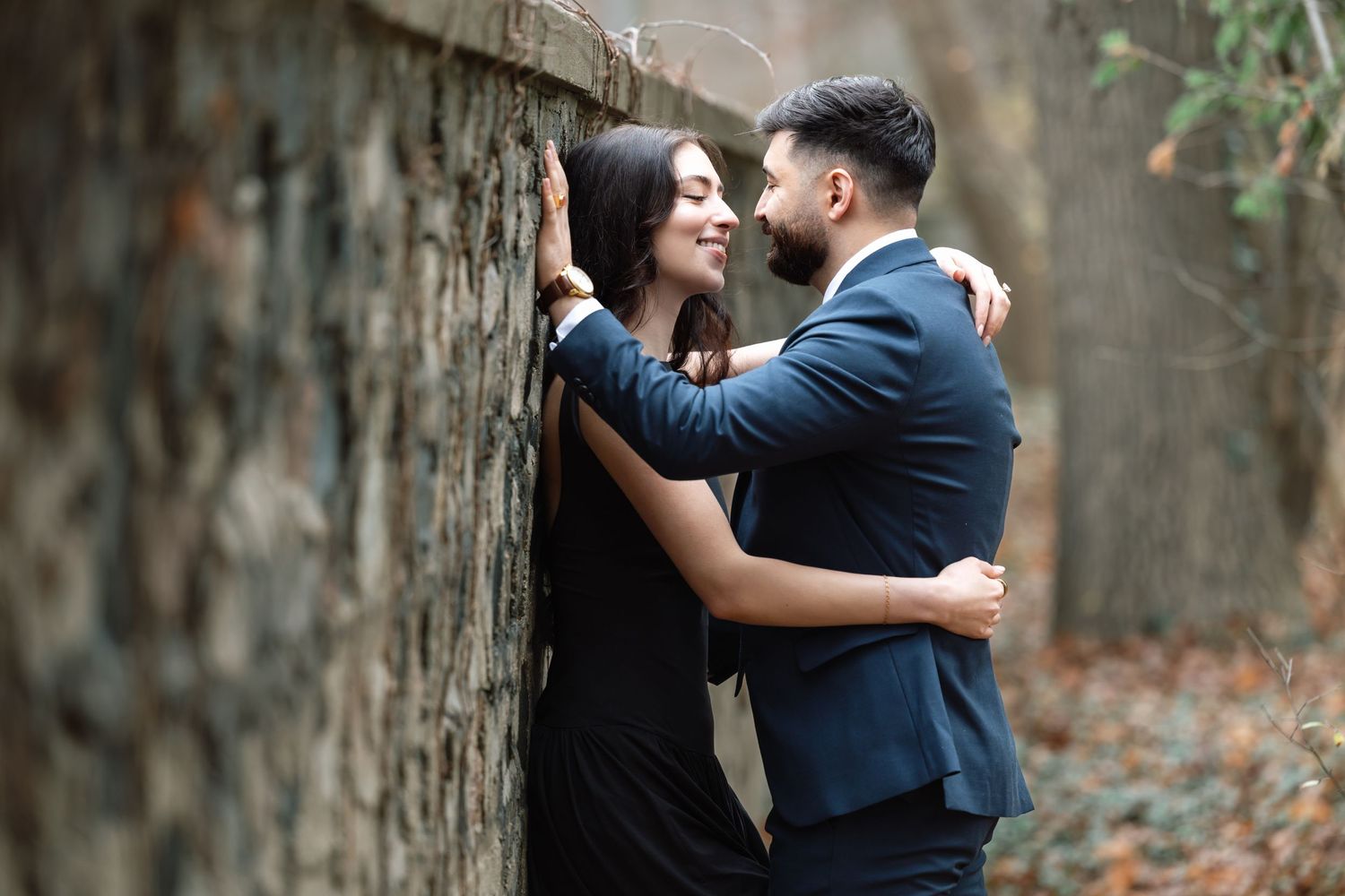 An intimate outdoor couple portrait with the pair embracing against a weathered stone wall.