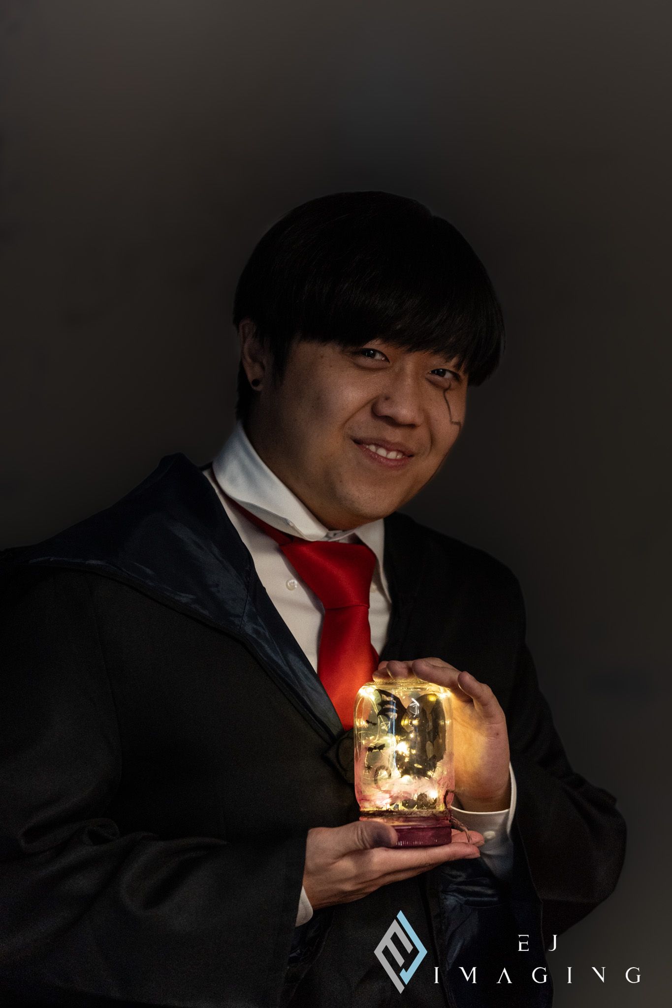 Portrait of someone in a dark suit and red tie holding a glowing illuminated glass sphere against a black background.