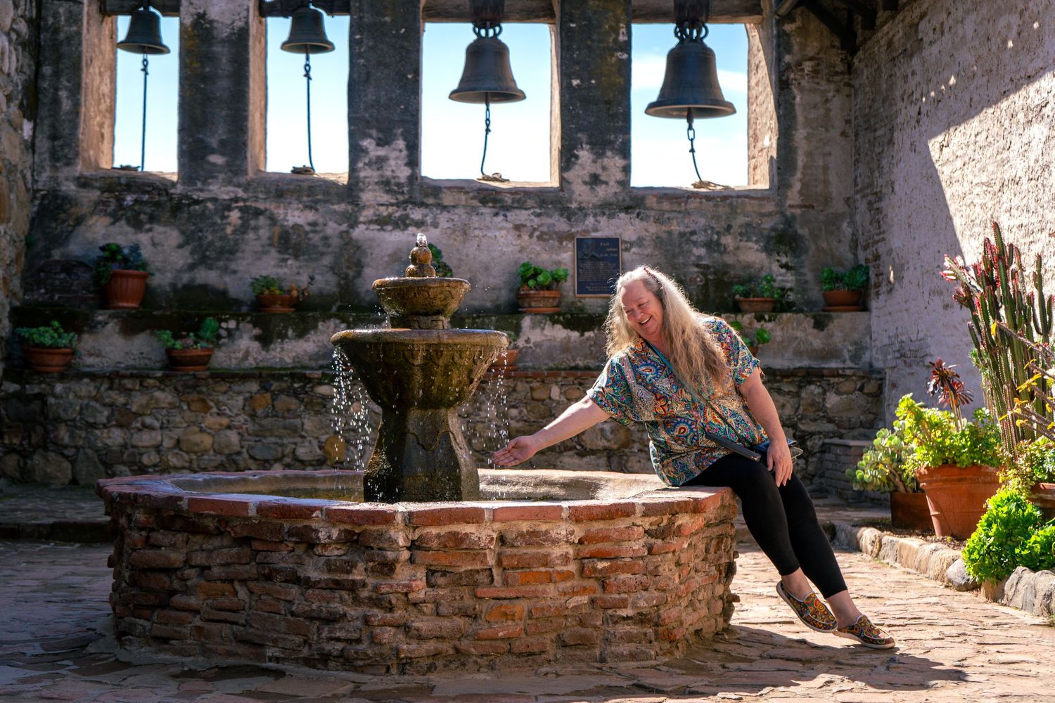 Historic bell tower with stone fountain in foreground and sunlit courtyard.
