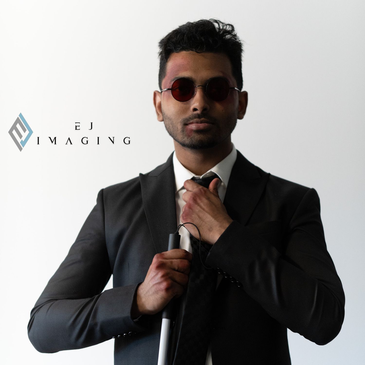 Professional wearing a black suit and red tie adjusts his necktie while posing against a light background with sunglasses.