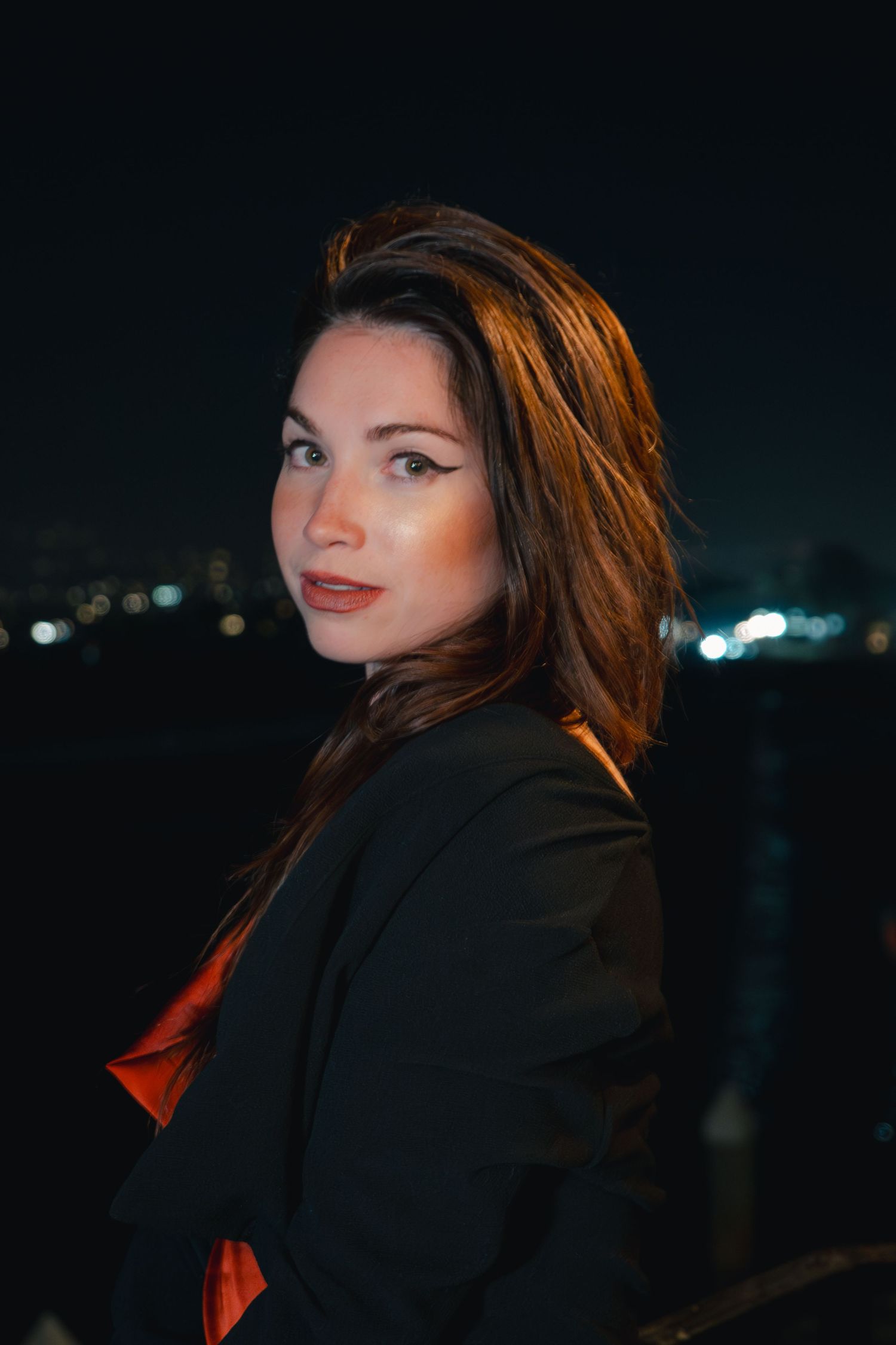Nighttime portrait of a model in black jacket with city lights in background.