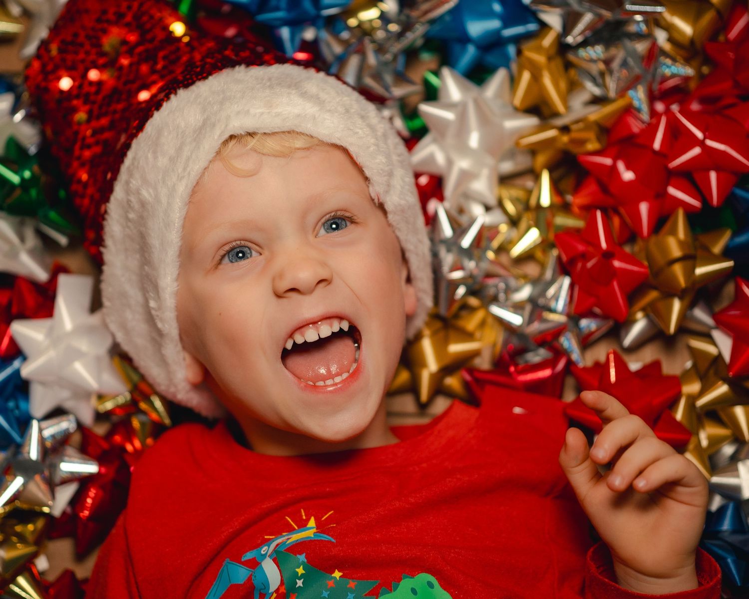 Young child in Santa hat surrounded by colorful Christmas gift bows.