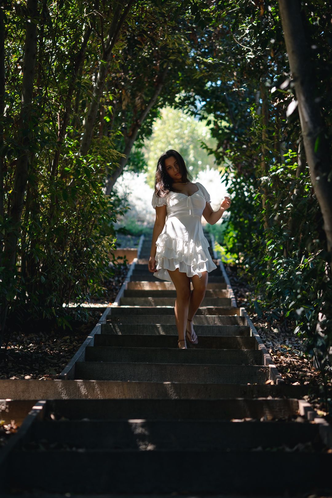 A white summer dress catches sunlight on outdoor wooden stairs surrounded by lush green trees and foliage.
