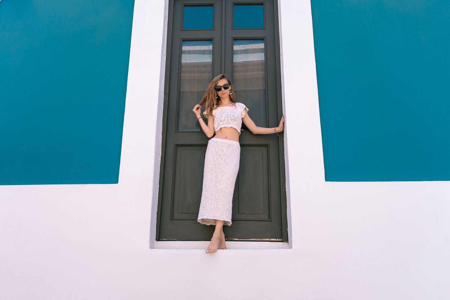 Someone in a pink dress poses in front of a dark green door against a turquoise and white building exterior.