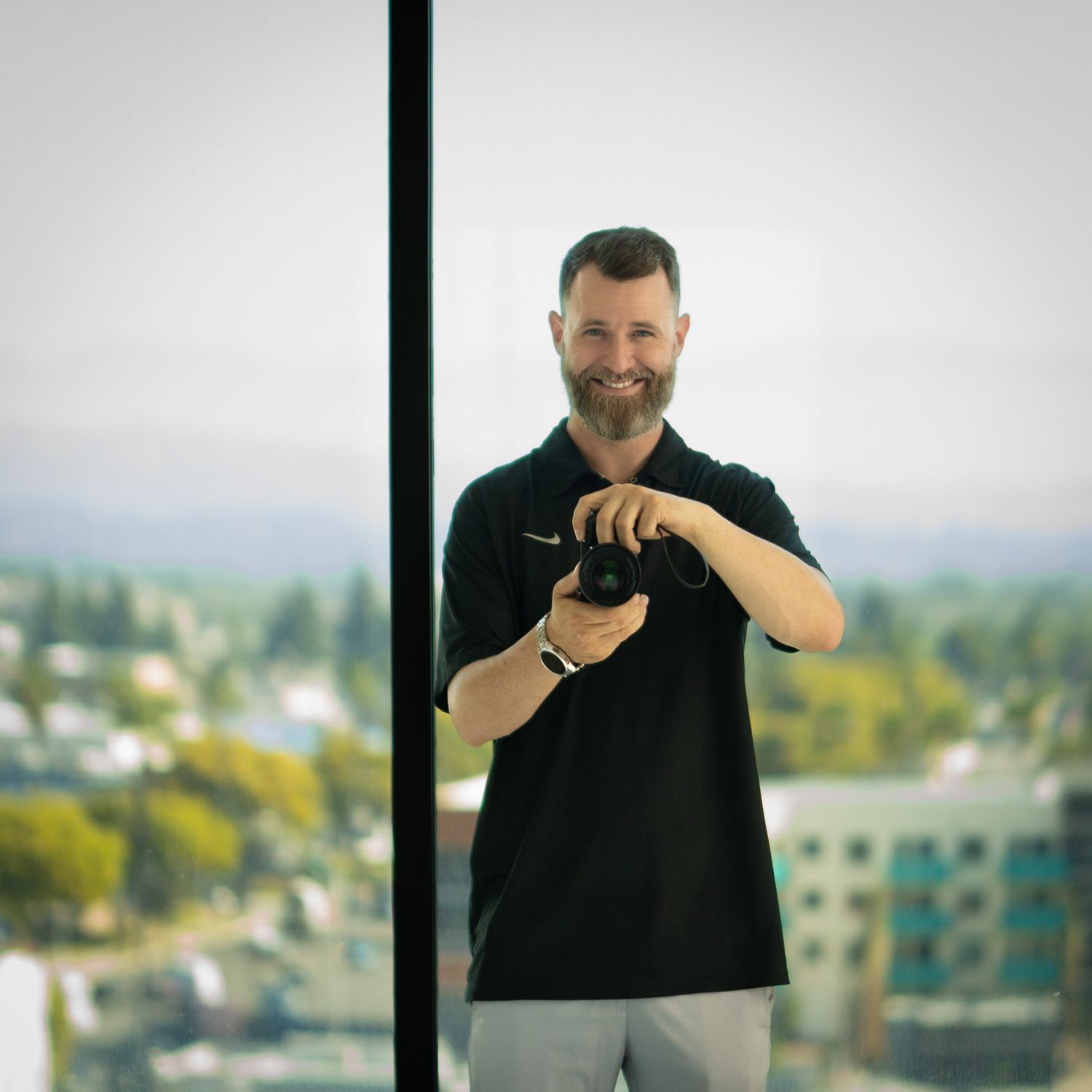 A photographer in black polo shirt using camera equipment against cityscape background.