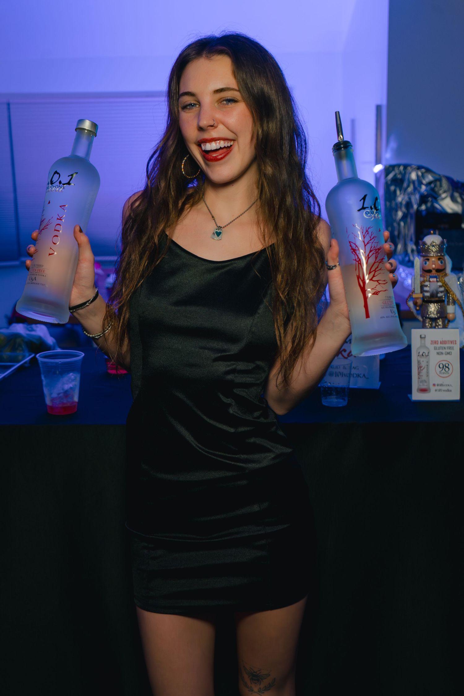 Bartender in black dress holding illuminated bottles at nightclub.
