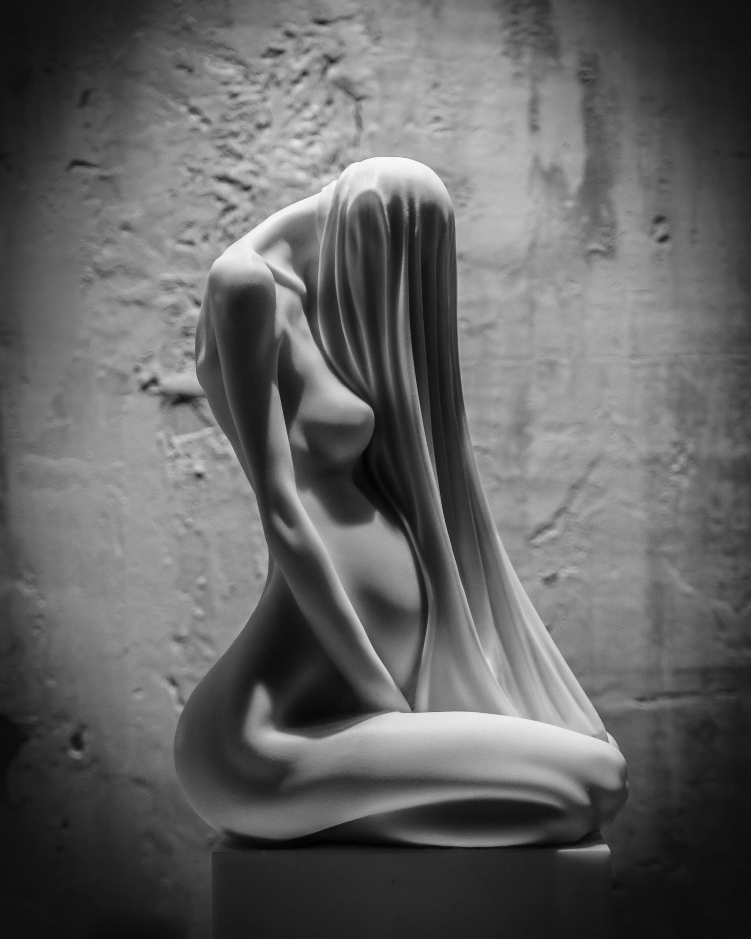 Artistic black and white sculpture of draped figure in contemplative pose.