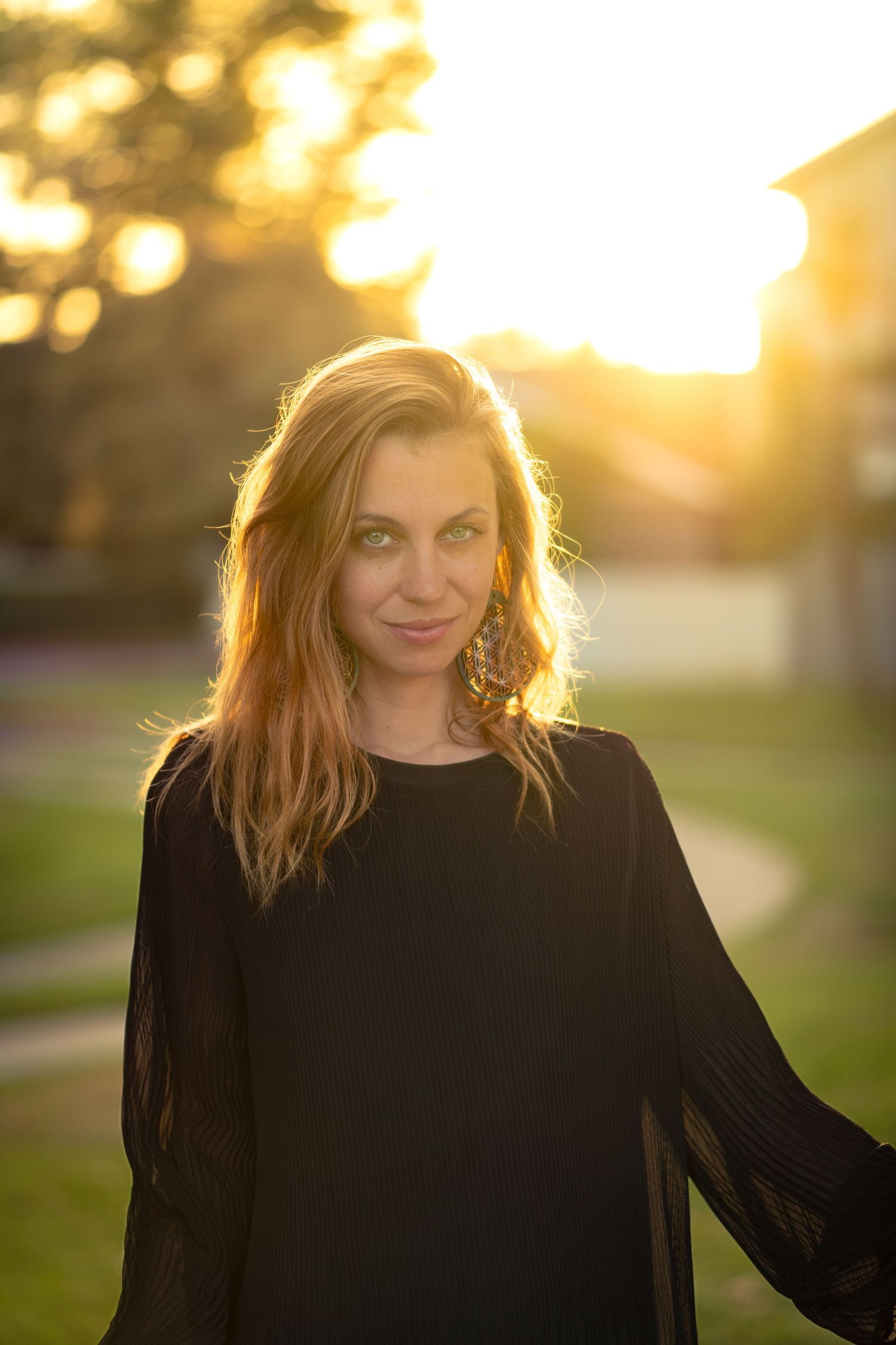 Backlit portrait at golden hour wearing flowing black top with dreamy bokeh background.
