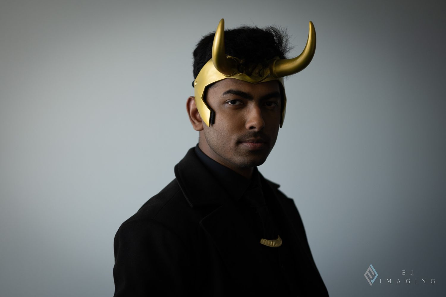 Studio portrait with gold horned headpiece against gray background.